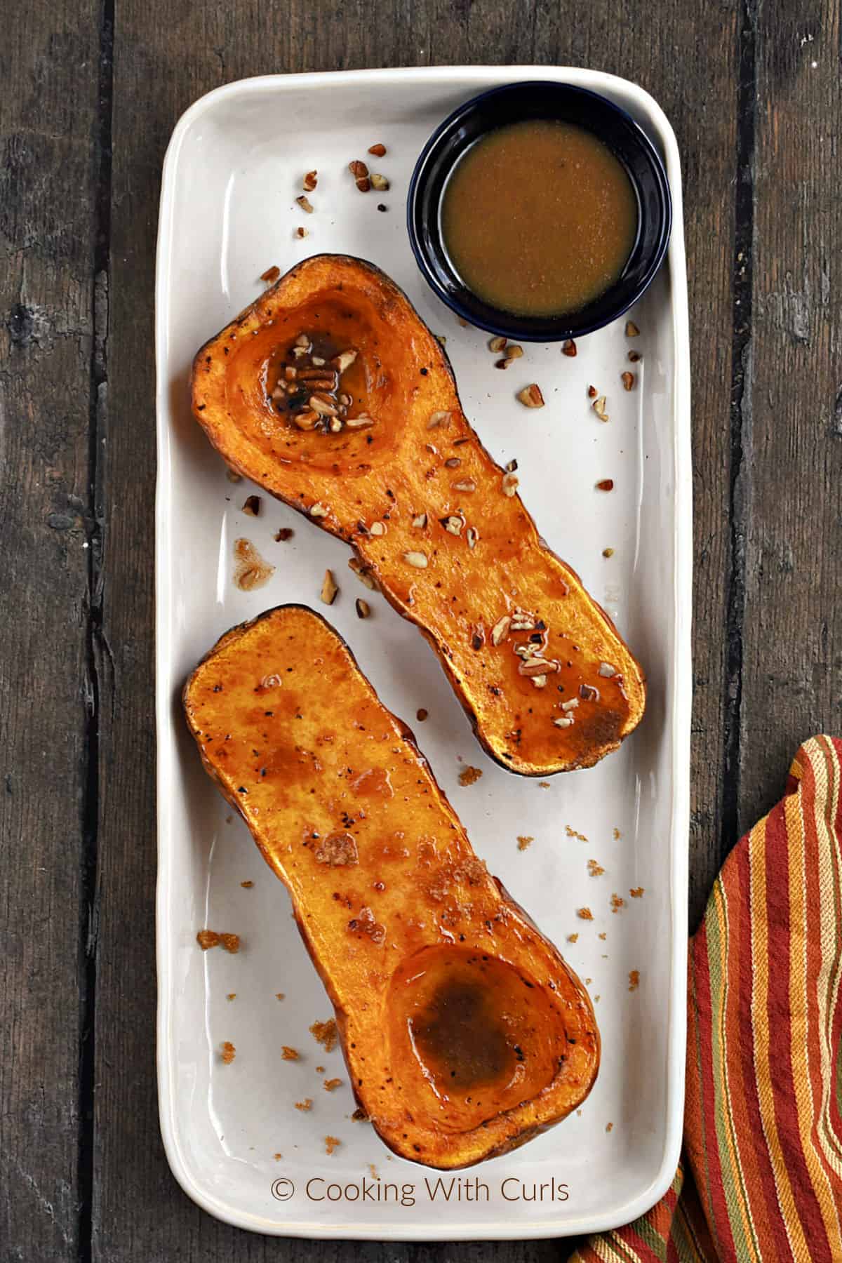 One air fryer butternut squash halves topped with maple syrup and pecans and the other with butter and brown sugar with a bowl of glaze on the side. 