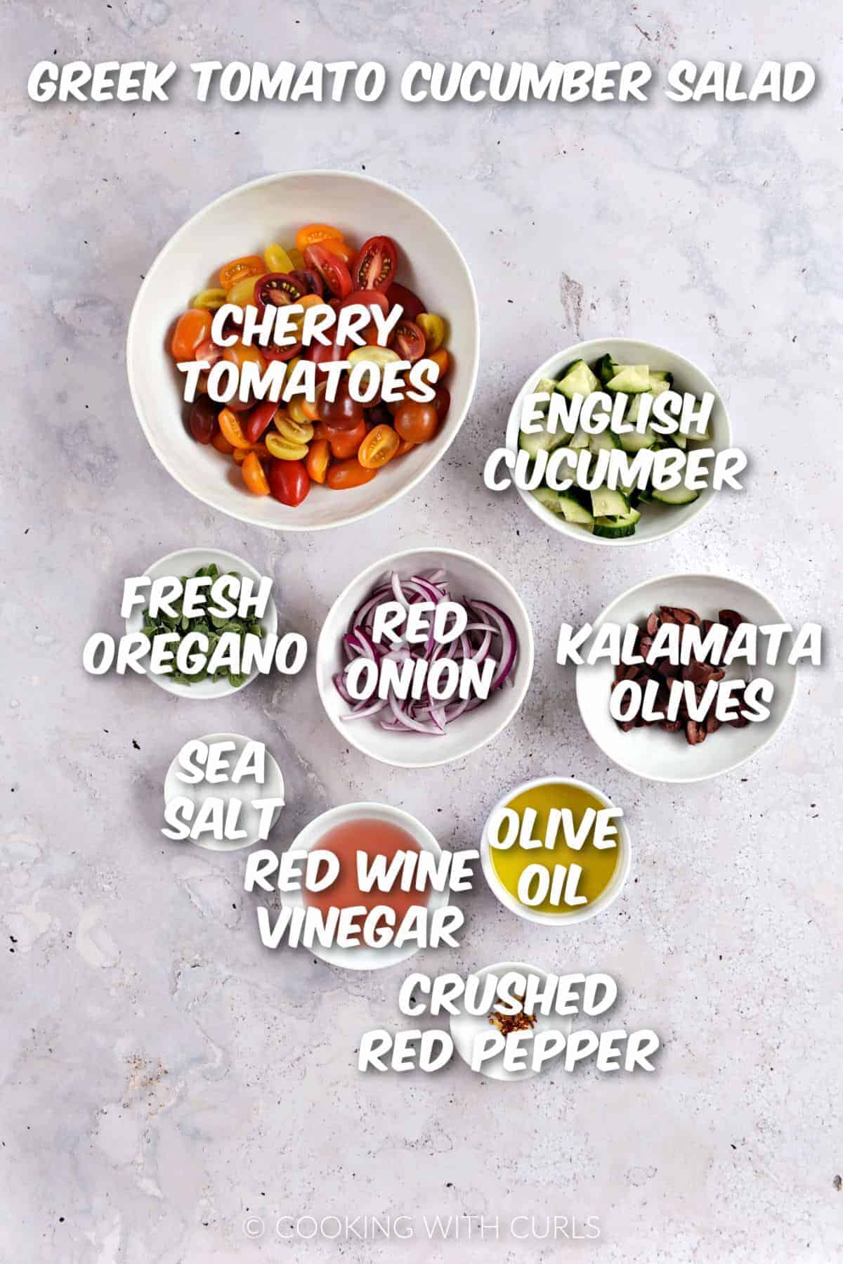 Sliced cherry tomatoes, cucumber, red onion, kalamata olives, oregano leaves, sea salt, red wine vinegar, olive oil, and crushed red pepper in white bowls. 