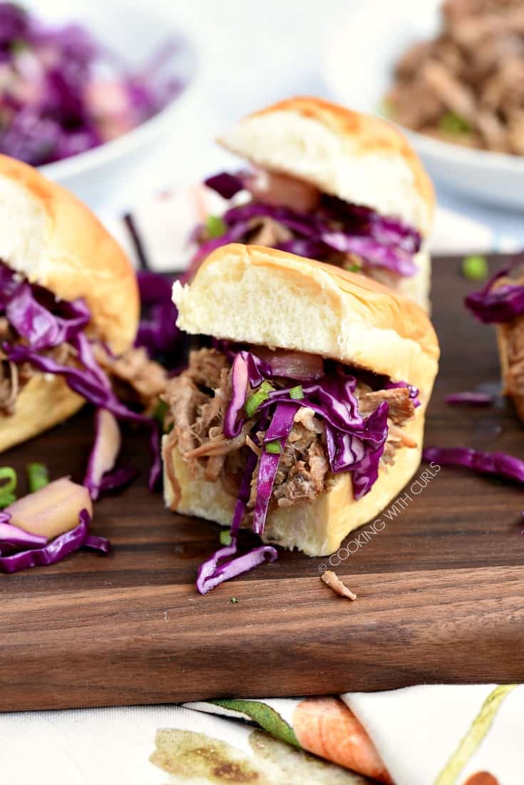 Hawaiian Pulled Pork sandwiches topped with pineapple slaw sitting on a wood board