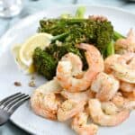 A large white plate topped with shrimp, lemon wedges and broccolini