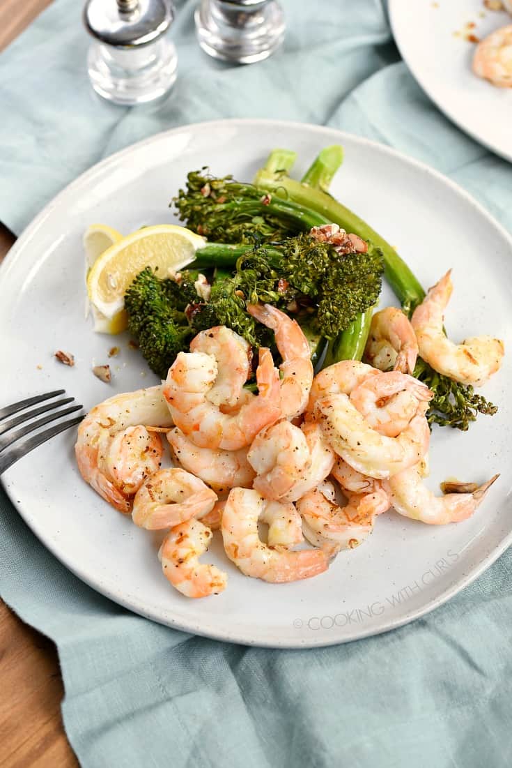 An overhead shot of shrimp, lemon wedges and broccolini on a large white plate