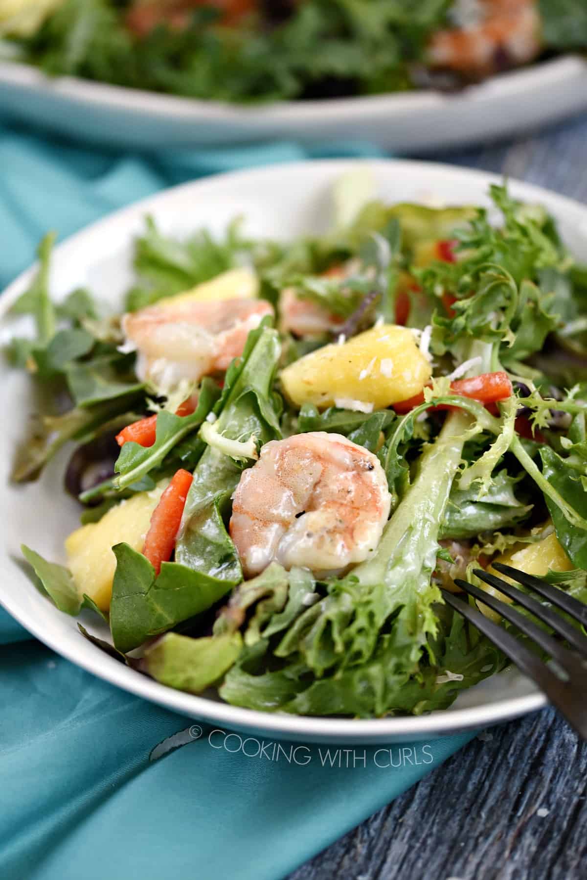 A close up image of a white bowl filled with salad greens, pineapple chunks, pepper strips and grilled shrimp drizzled with pina colada vinaigrette.