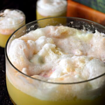 a big, glass punch bowl filled with bubbly and foamy polyjuice potion with two glasses filled with potion in the left corner and a stack of harry potter books in the right hand corner.