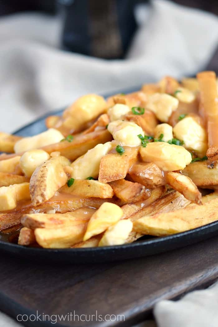 French fries and cheese curds topped with brown gravy in an oval cast iron skillet.