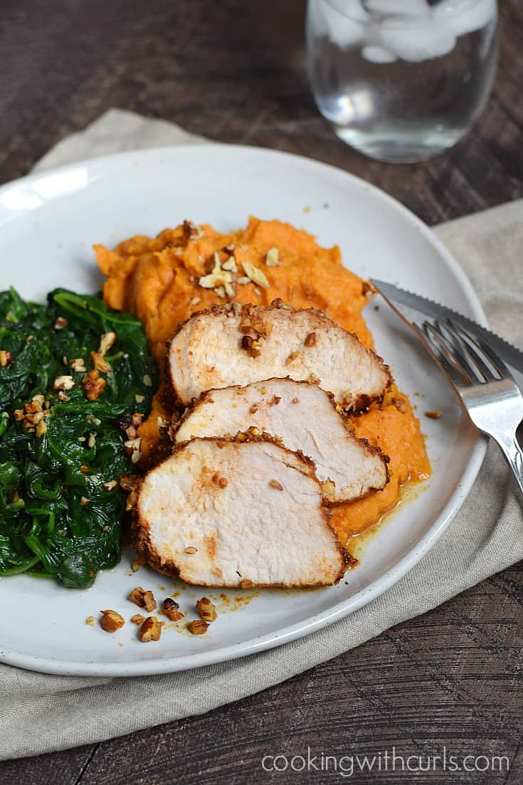 Pecan-Crusted Pork Tenderloin slices on a bed of mashed sweet potatoes next to sautéed spinach. 