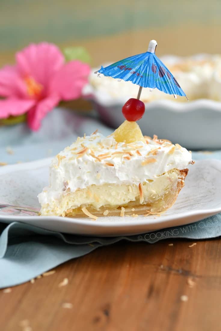 A slice of Pina Colada Pie on a wavy plate topped with a cherry and blue cocktail umbrella