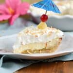 Side view looking at a slice of PIna Colada cream Pie topped with a cherry and blue cocktail umbrella