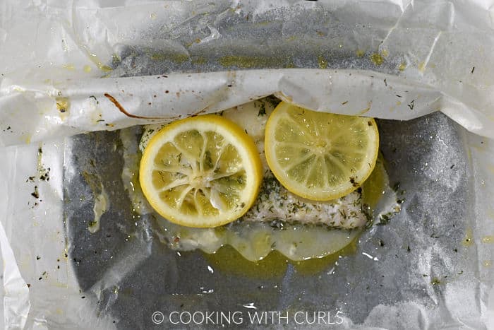 A baked cod filet in parchment paper opened up on a black plate. 