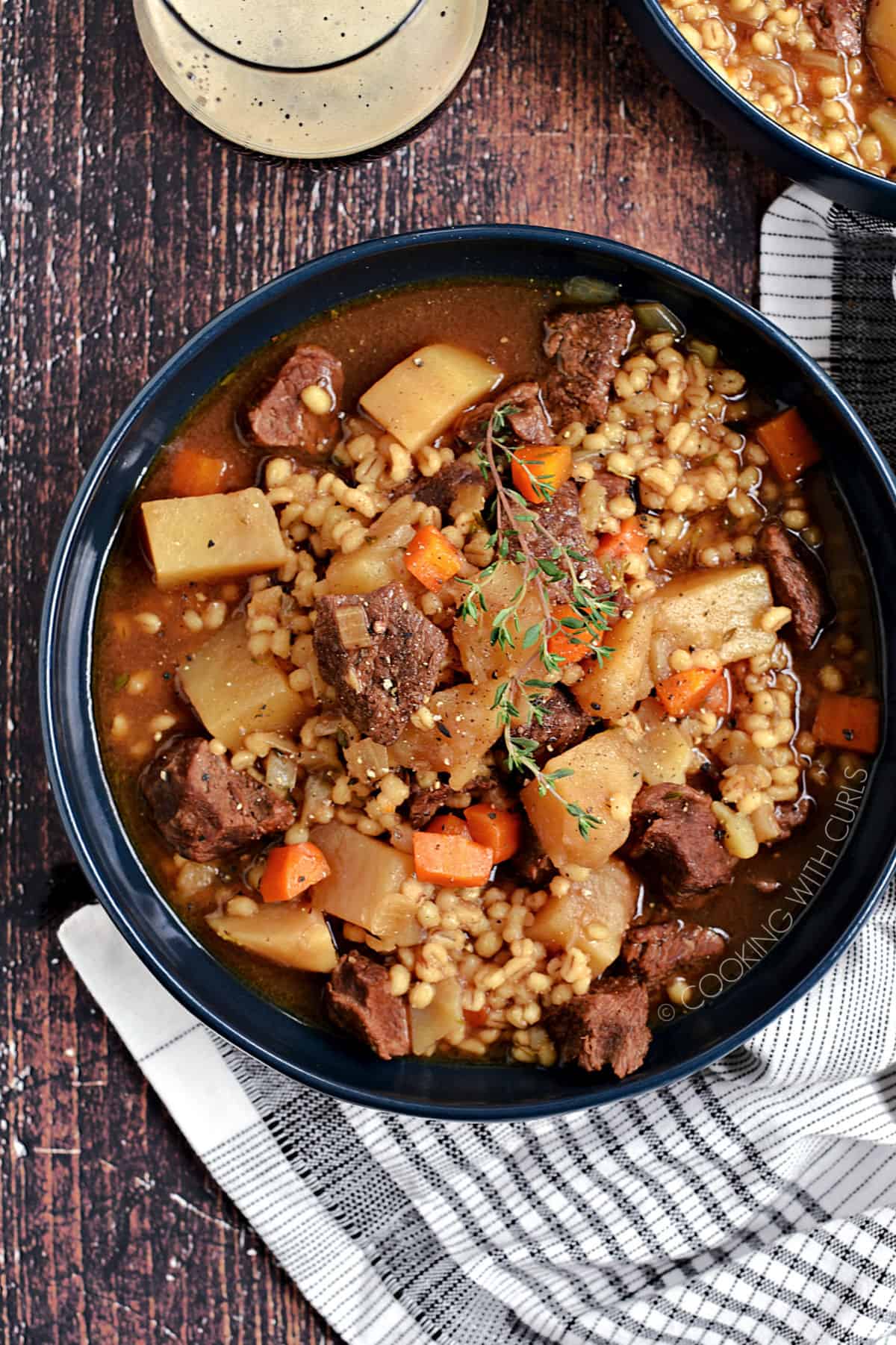 Looking down on a big blue bowl of beef, potato and carrots chunks surrounds by broth and barley.