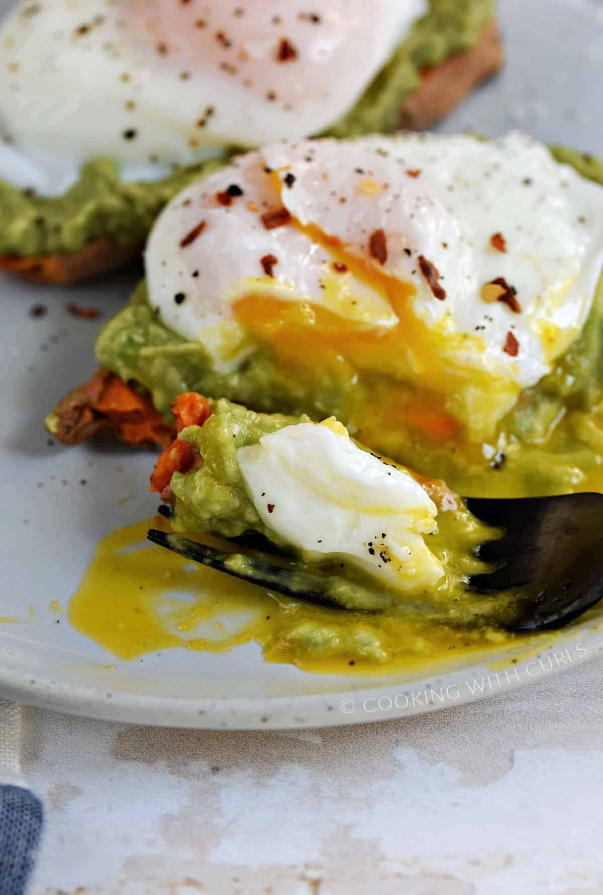 A fork sliced through the poached egg, avocado, and sweet potato and resting on a plate.