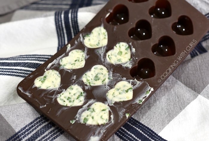 A brown, silicone heart-shaped mold with eight herb-butter filled cavities. 