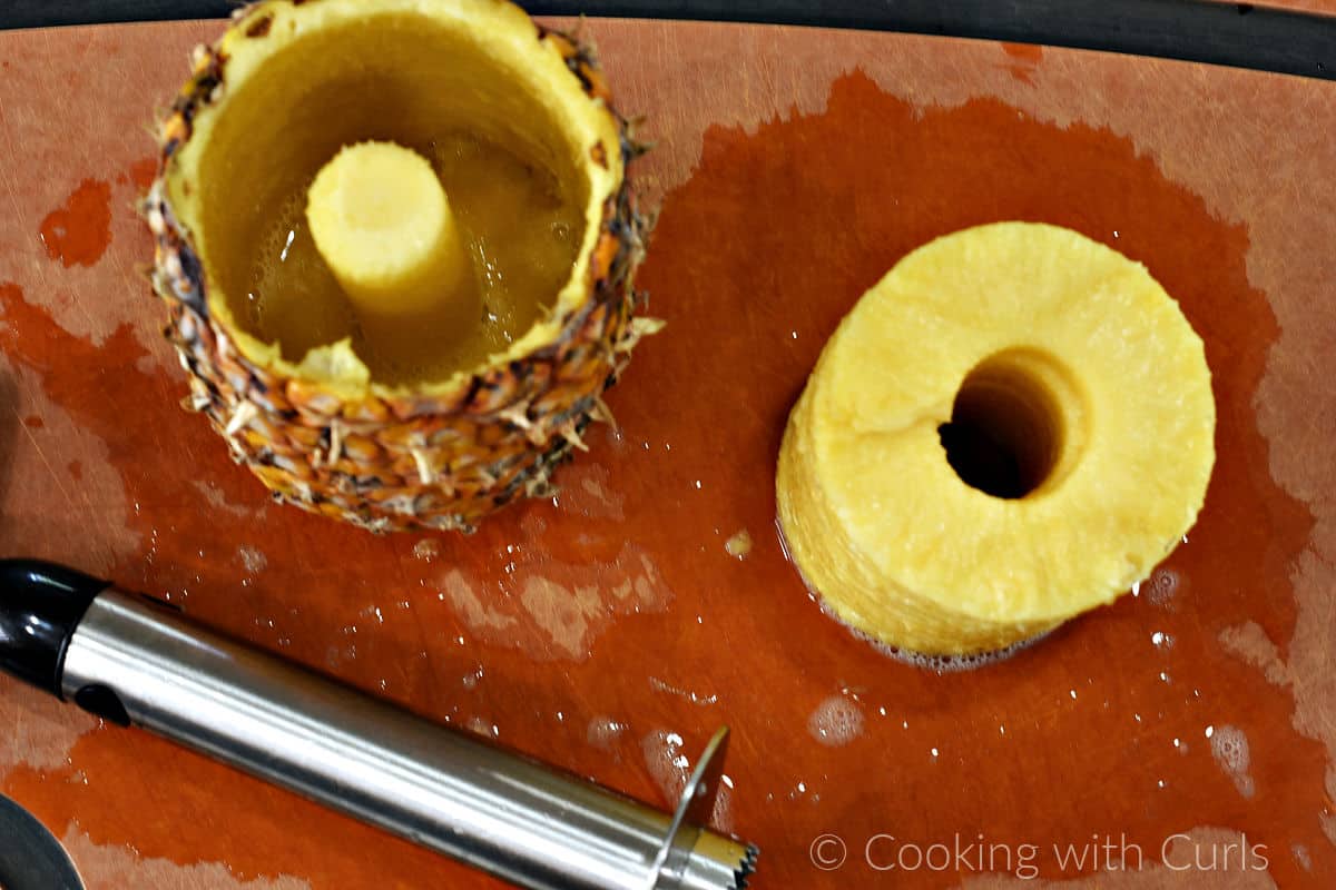 A fresh pineapple sliced and cored with a tool on a cutting board. 