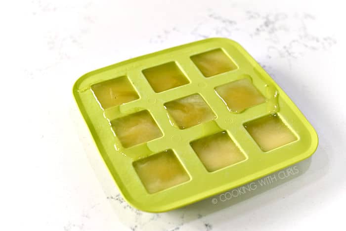 a green silicone ice cube tray filled with six square sections of frozen pineapple juice. 