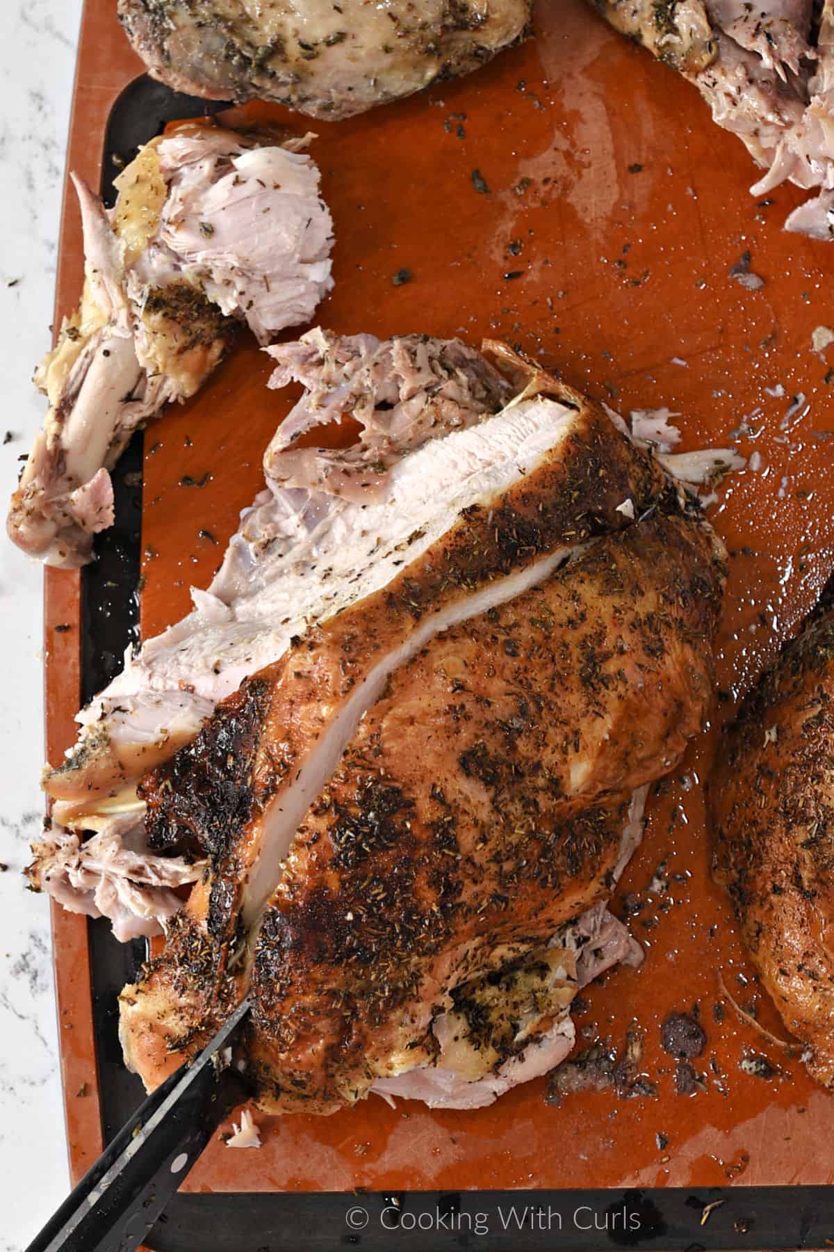 A knife cutting between the breast meat and rib cage on a cutting board.