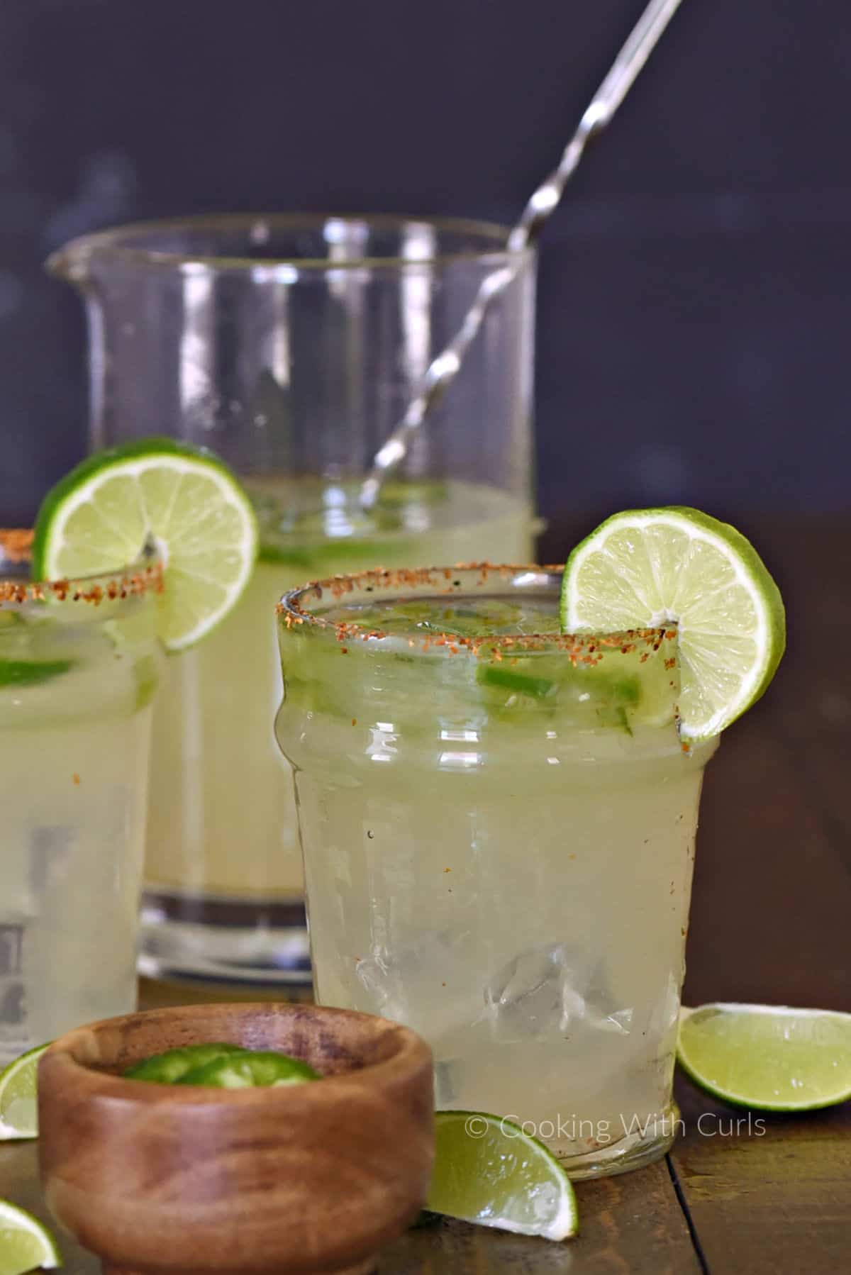 A pitcher and two glasses of spicy jalapeno margarita with chili pepper rim and lime wheels for garnish. 