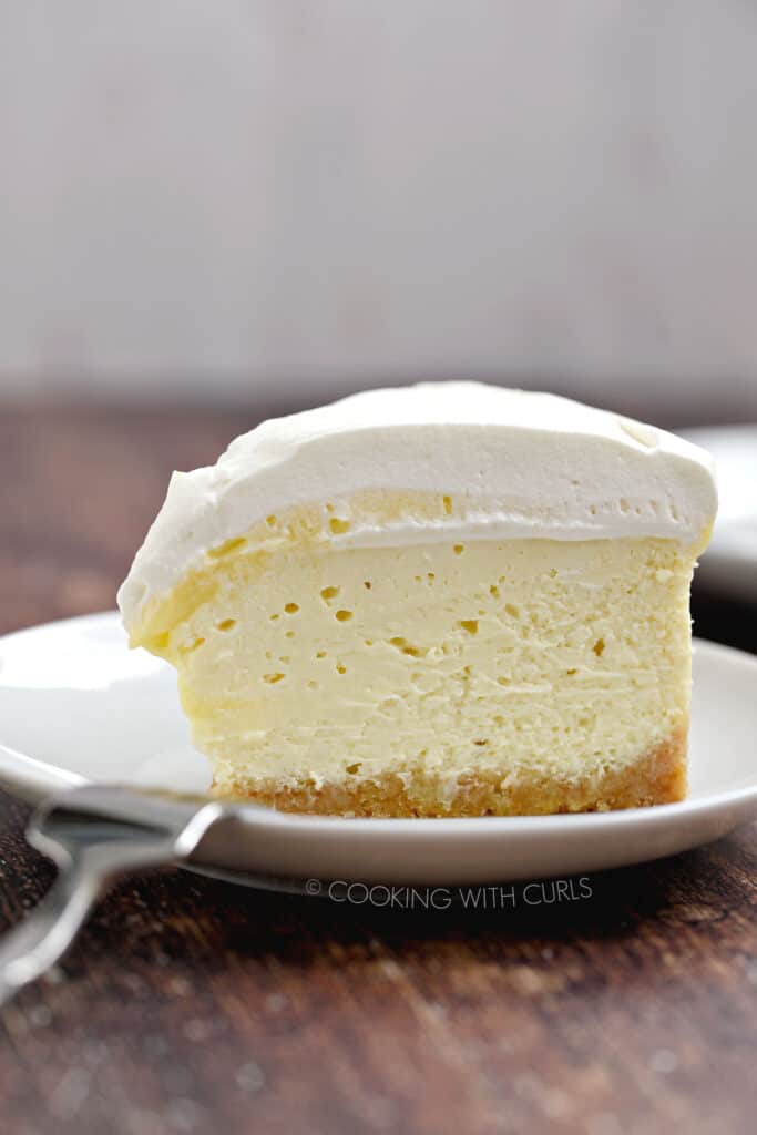 A slice of Instant Pot Lemon Cheesecake on a small white plate with a fork laying on the edge.