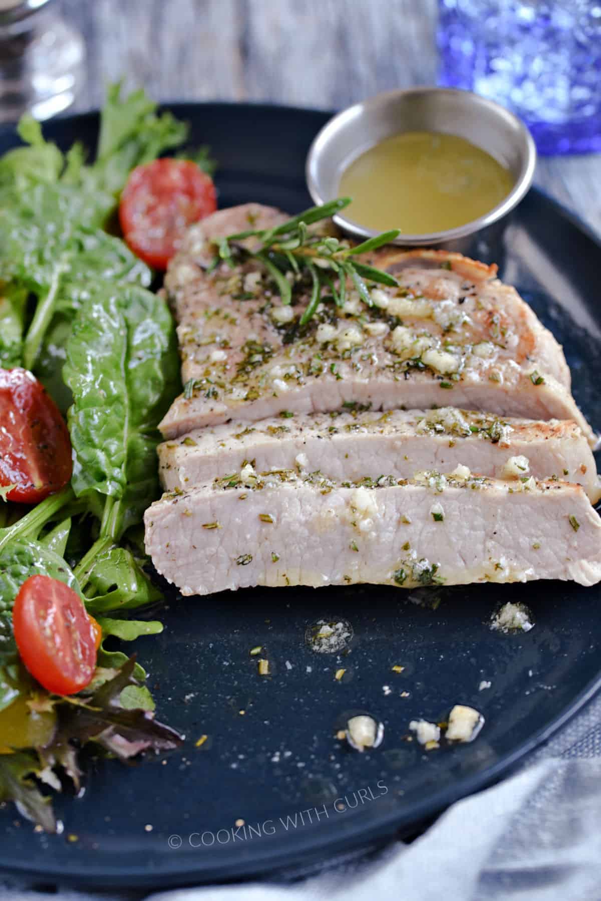 A sliced pork chop topped with melted garlic rosemary butter with a green salad on the side.