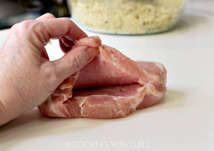 A slit cut into the side of a thick pork chop on a white cutting mat. 