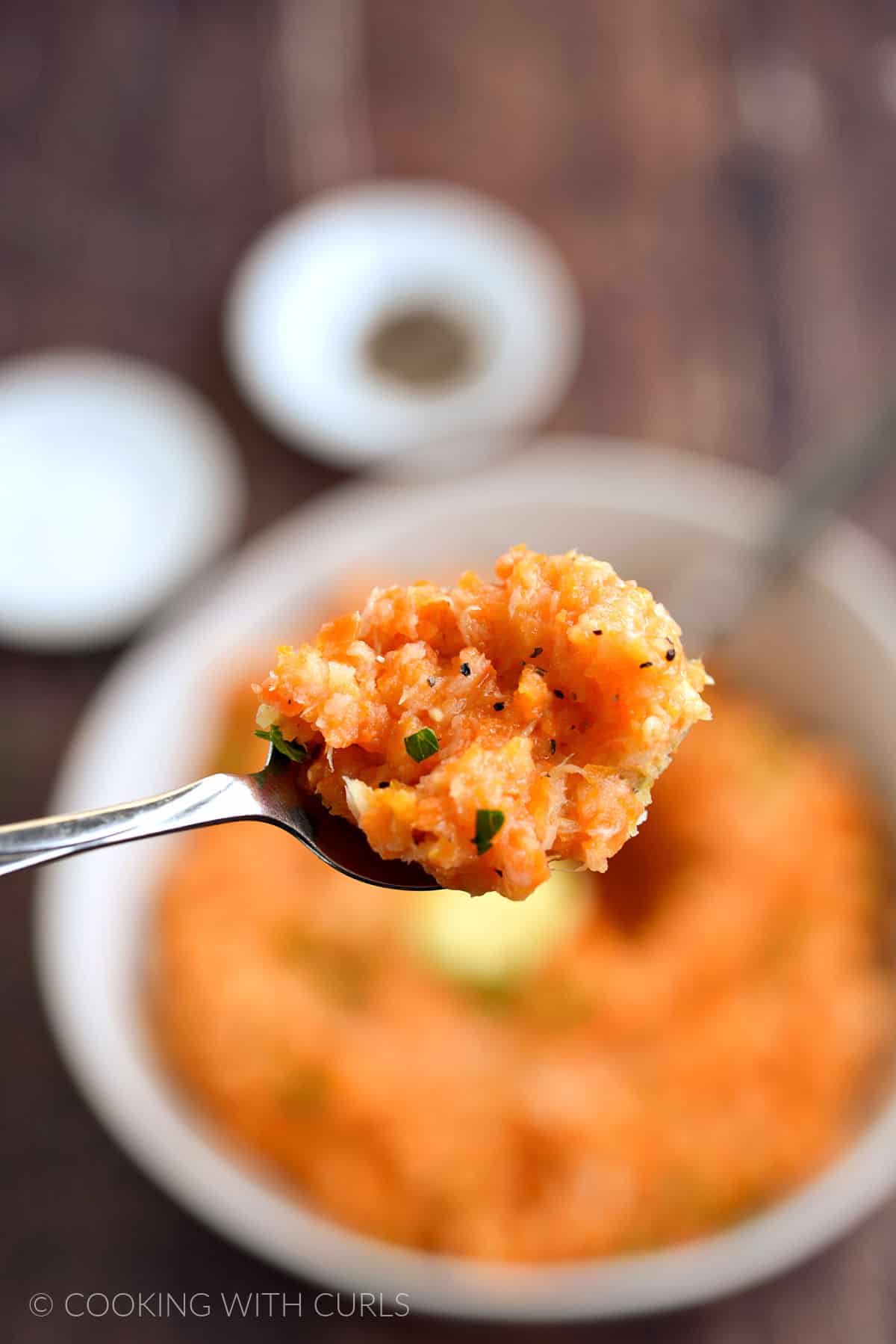 A spoonful of mashed carrots and parsnips held above the bowl. 