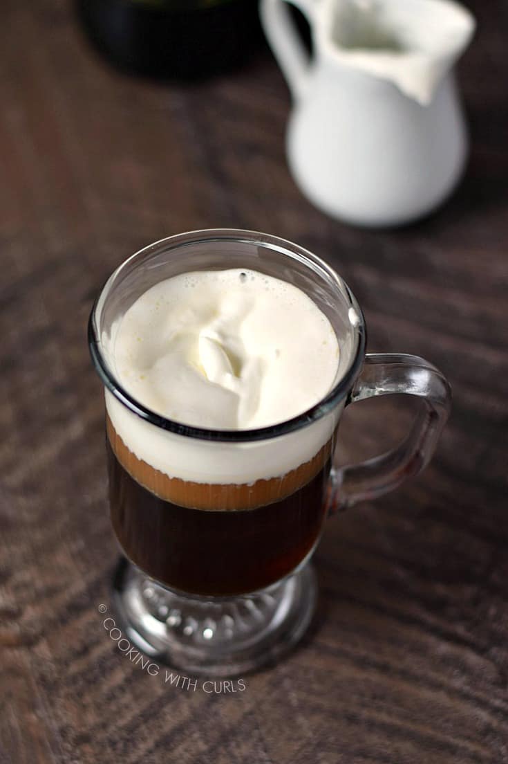Looking down on an Irish Coffee in a traditional glass mug with a creamer pitcher in the upper right corner
