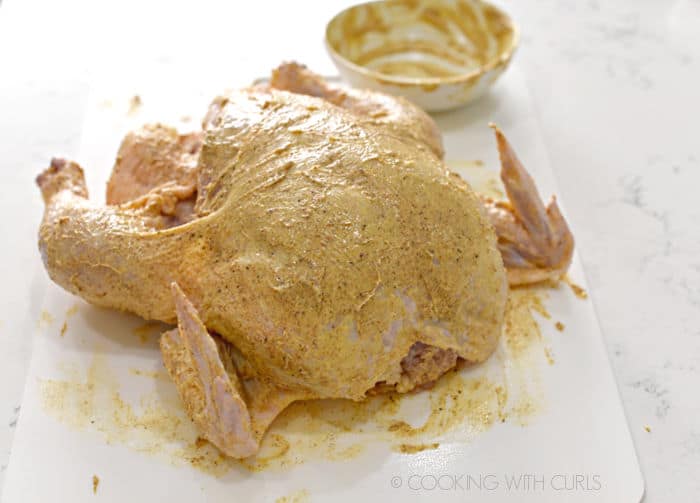 A whole chicken on a white cutting mat rubbed with seasoned butter. 