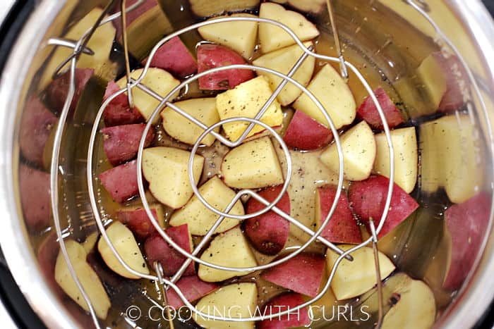 A wired rack laying on top of chicken stock, quartered red potatoes, butter, salt and pepper. 