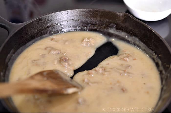 a wooden spoon pulling through the thickened gravy in a cast iron skillet. 