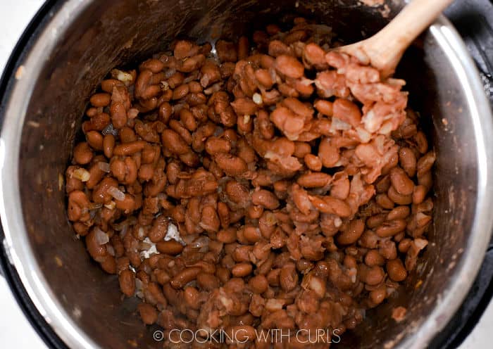 A wooden spoon stirring the drained beans into the sautéed onion and garlic. 