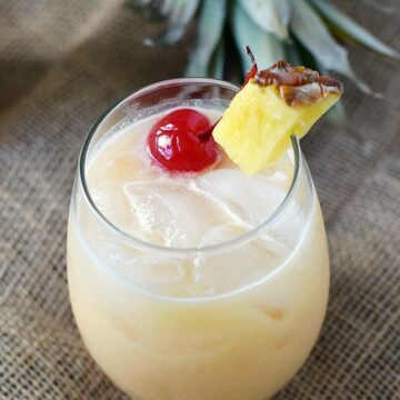 A small glass filled with coconut milk, pineapple juice and rum garnished with a pineapple wedge and cherry.