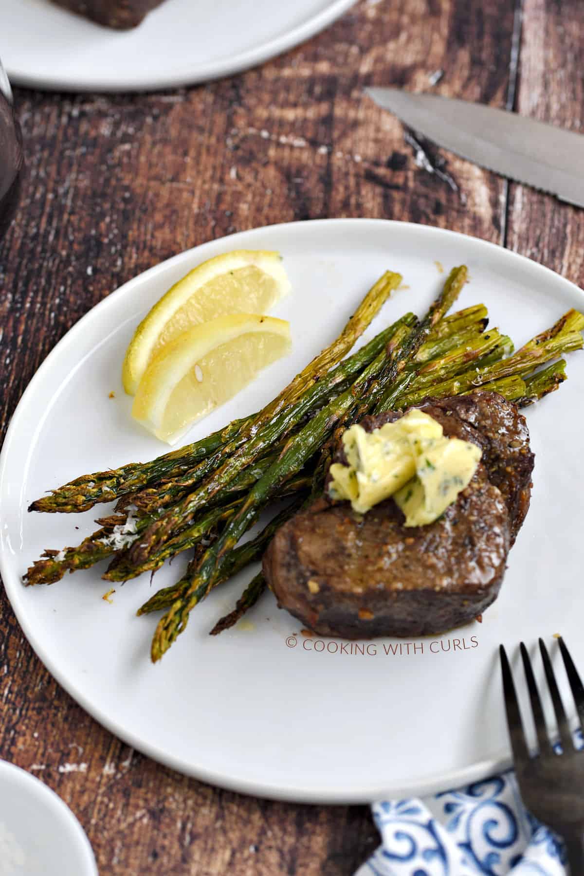 Air Fryer Steak and Asparagus topped with garlic butter and lemon wedges on a white plate. 