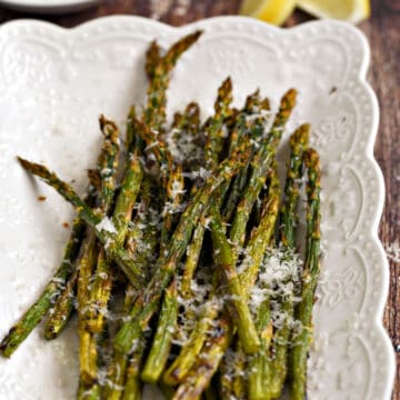 Asparagus spears topped with lemon zest and parmesan cheese laying on a white platter.