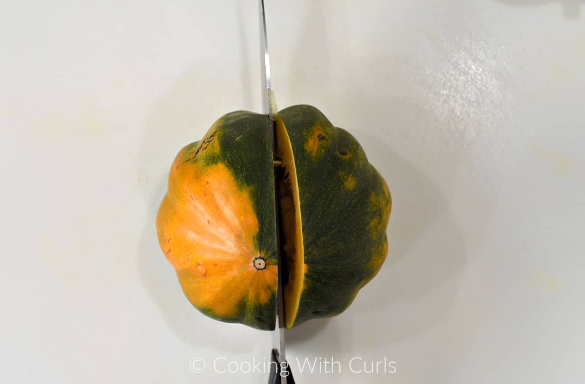 An acorn squash cut in half with a chefs knife on a cutting board. 