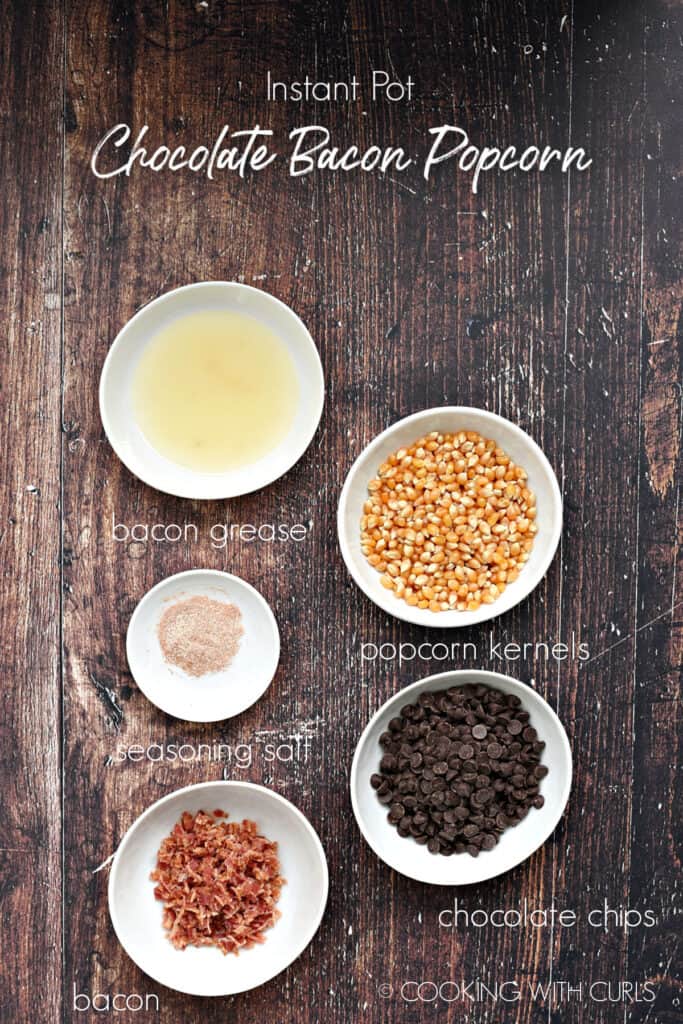 Bacon grease, popcorn kernels, seasoning salt, chocolate chips and bacon in small white bowls on a wooden background. 