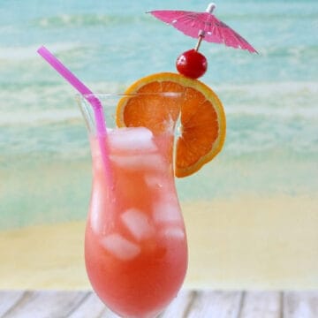Bright red cocktail in a hurricane glass with an orange slice, cherry, pink paper umbrella, and purple straw.