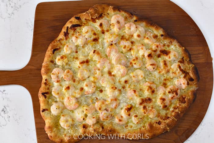 Baked garlic shrimp pizza on a wooden pizza peel. 