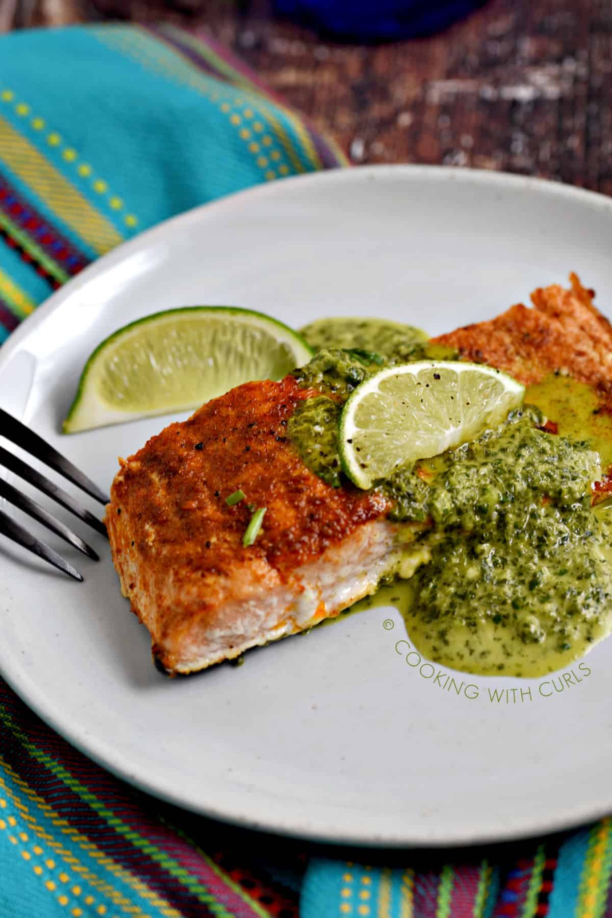Baked Salmon topped with Cilantro Lime Sauce on a white plate with a lime wedge on the side.