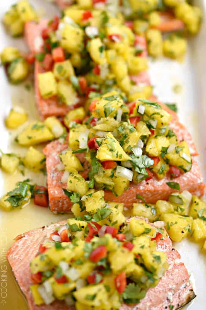 Close-up image of pineapple salsa topped salmon fillets on a white platter.