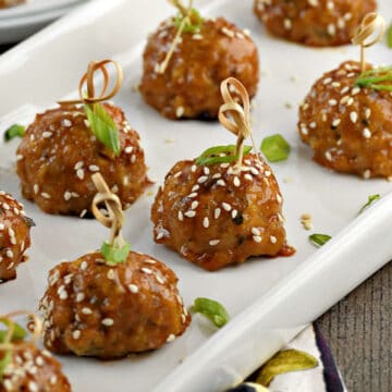 Chicken teriyaki meatballs on a platter with sesame seeds and green onion slices.