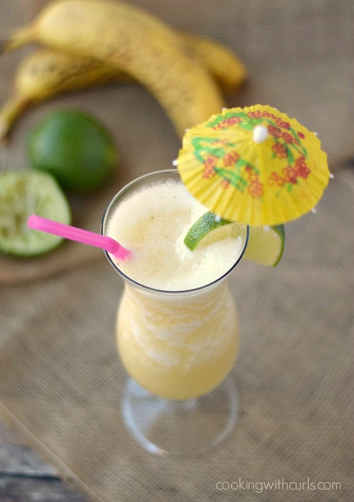 Looking down on a Frozen Banana Daiquiri garnished with a paper umbrella, pink straw and lime wedge.