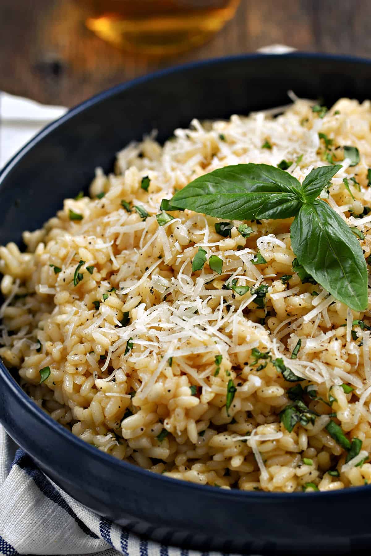 A large bowl filled with Basil Risotto topped with shredded Parmesan cheese and fresh basil leaves.