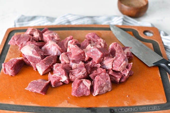 Beef chuck cut into cubes with a sharp knife on a cutting board.