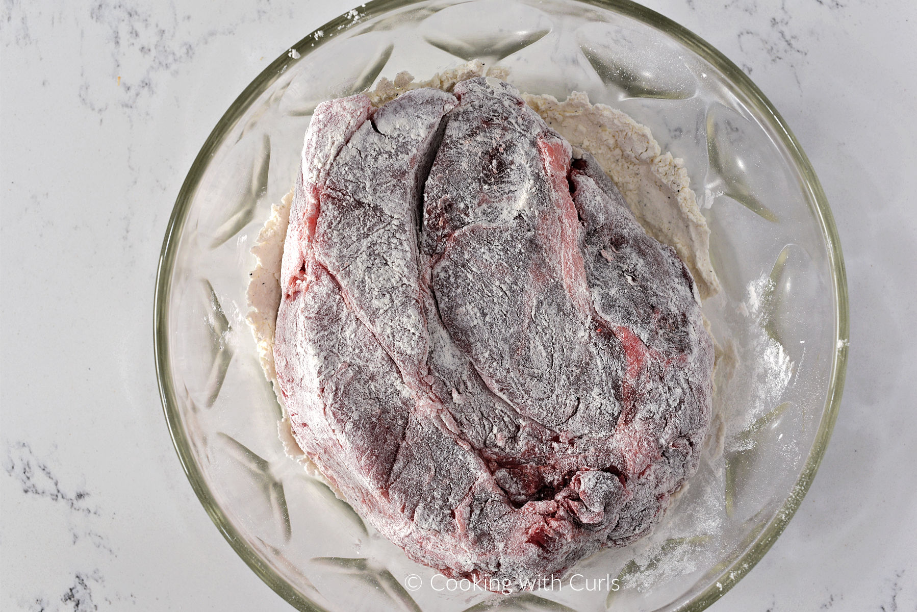 Beef Chuck roast coated in seasoned flour in a large bowl. 