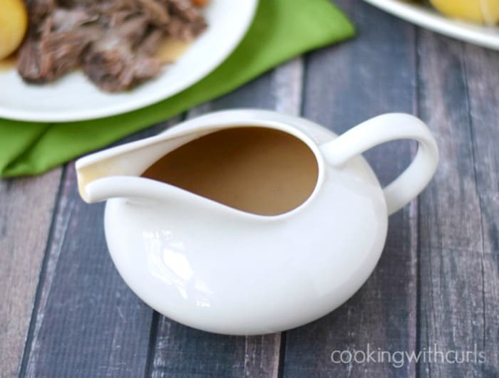 white gravy boat filled with beef gravy with a plate of pot roast in the background