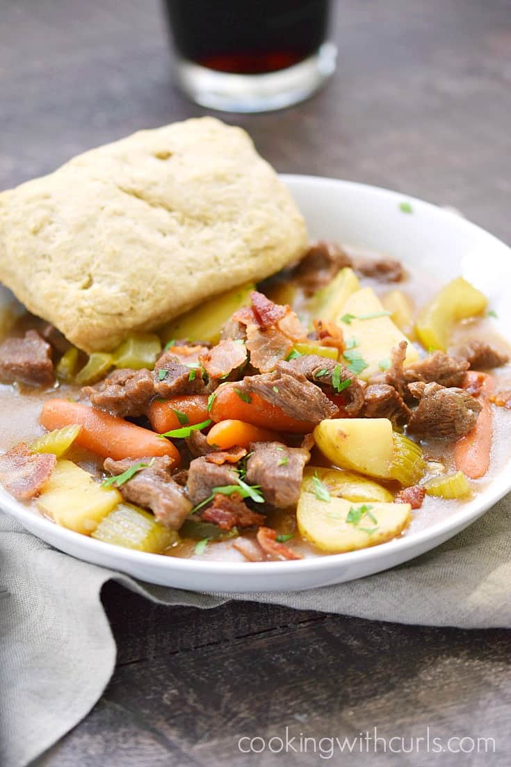 Beef Stew with Guinness Biscuits in a white bowl with a glass of Guinness in the background