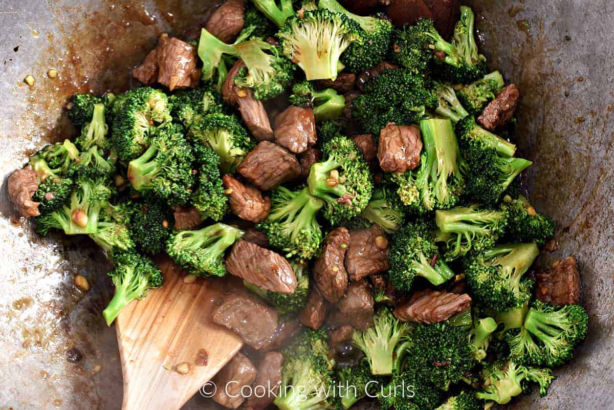 Beef strips, broccoli florets, and sauce tossed together in a wok. 
