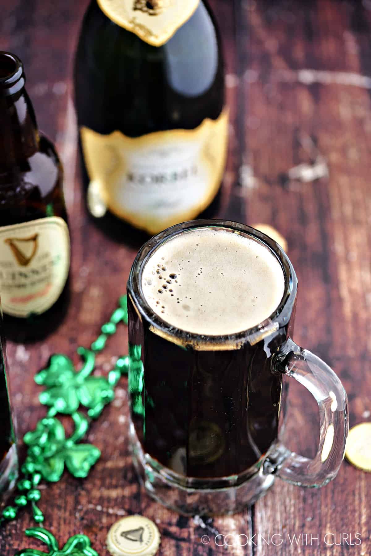 Foamy, black cocktail in a glass beer mug with bottles of Guinness and champagne in the background.