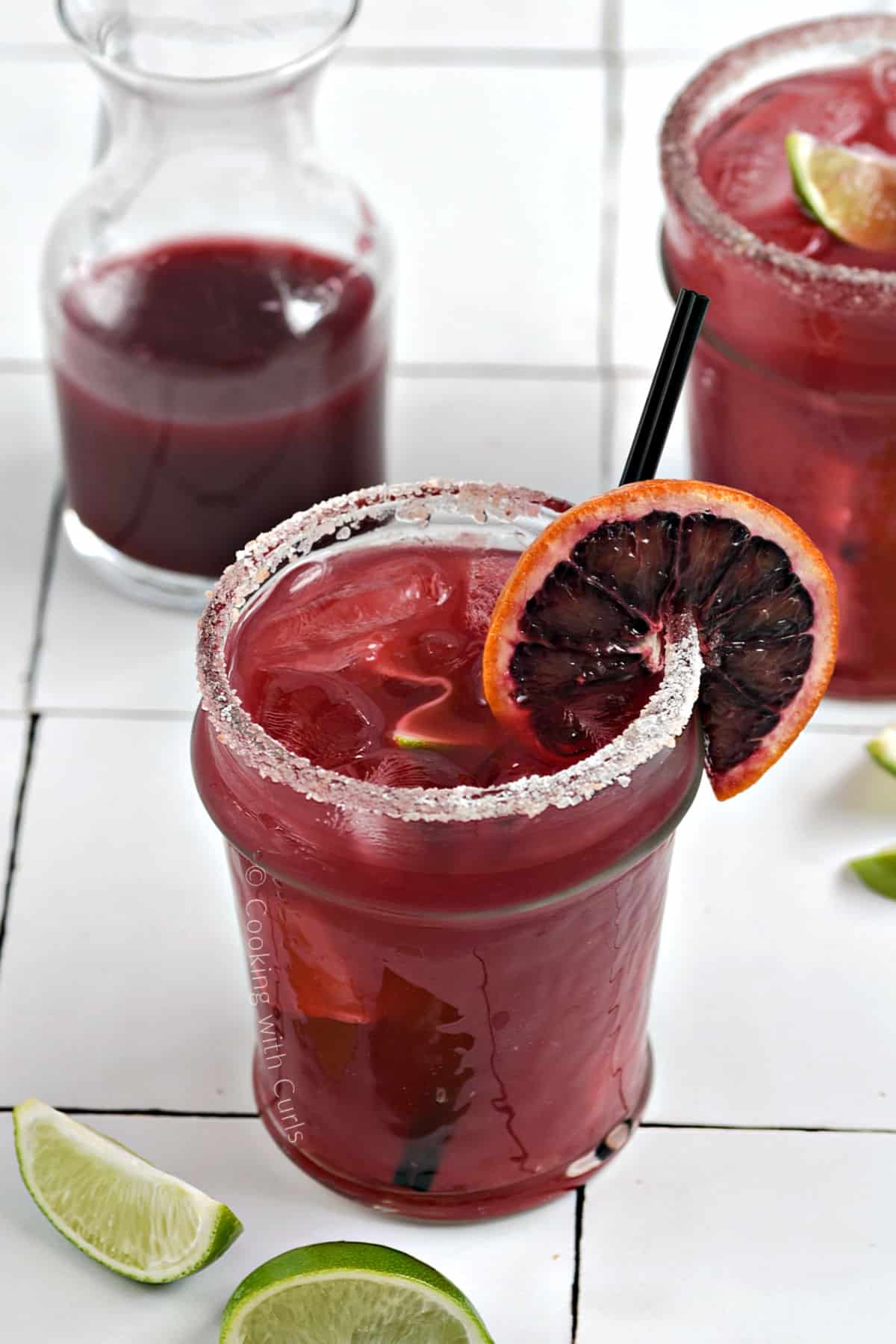 Looking down onTwo blood orange margaritas in short glasses garnished with an orange wheel and a sugar rim.