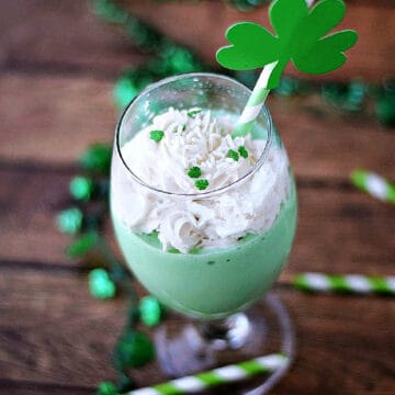 Whipped cream topped boozy shamrock shake with shamrock straw and sprinkles.