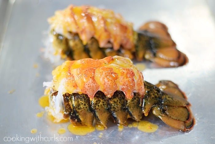 Garlic butter poured over the top of two, raw lobster tails on a baking sheet.
