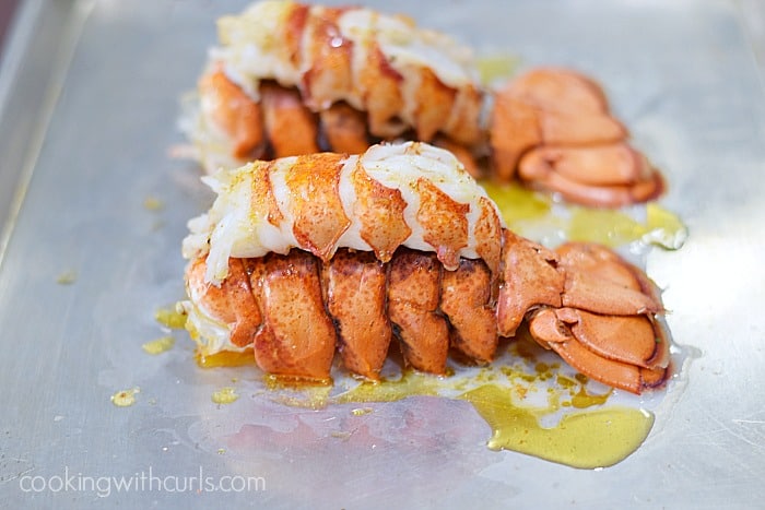 Two bright pink colored broiled lobster tails on a baking sheet.